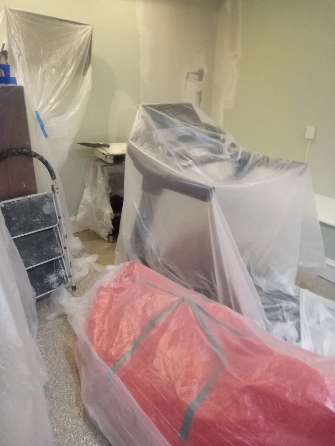 Room with furniture and floor covered in plastic sheeting before painting