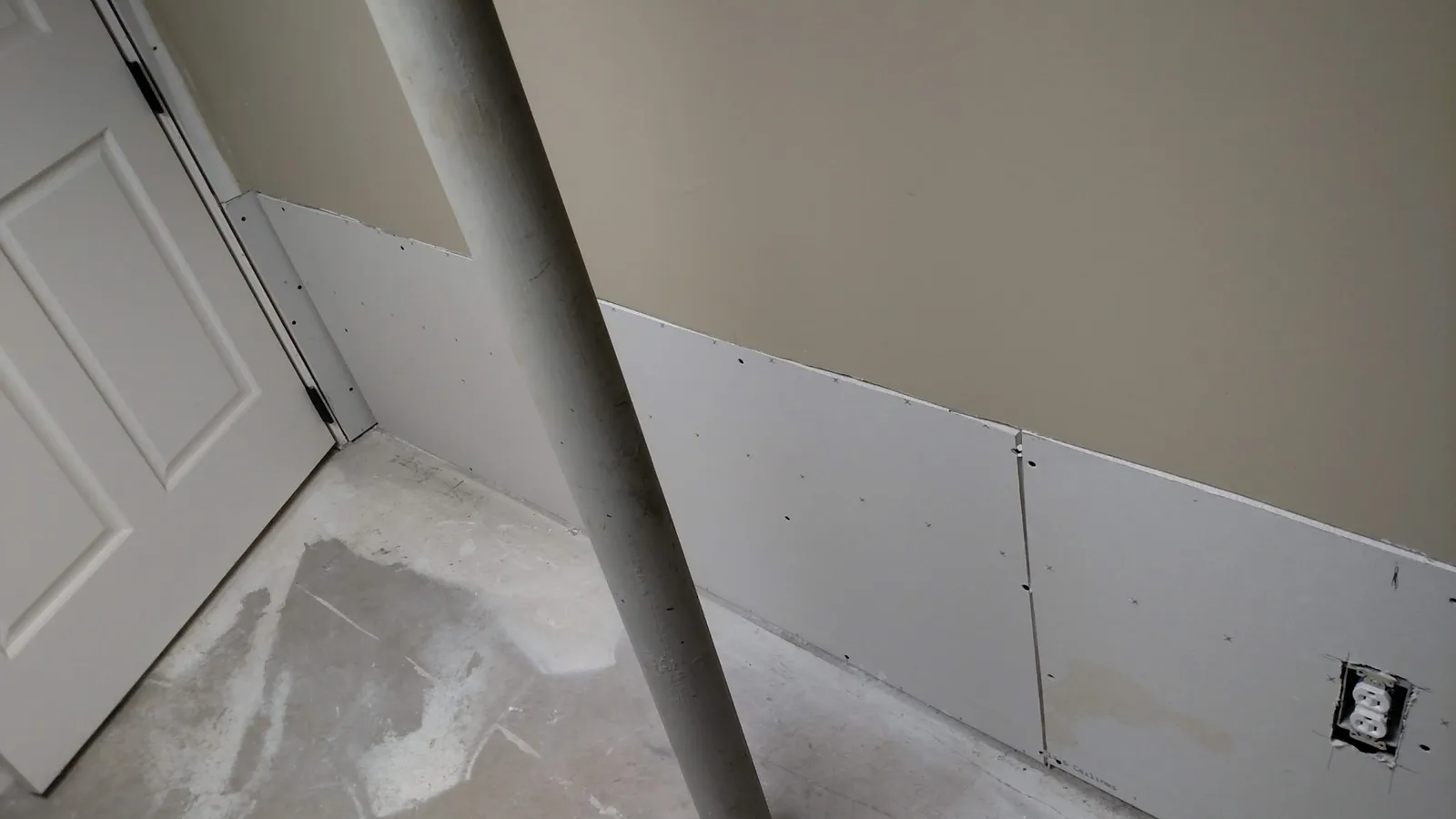 New drywall panels on a basement wall behind a steel support post